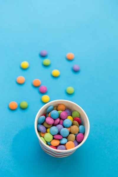 Caramelos gotas en taza de papel sobre fondo azul —  Fotos de Stock