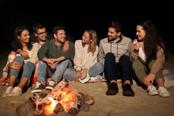 Groep vrienden zittend op kampvuur op het strand — Stockfoto