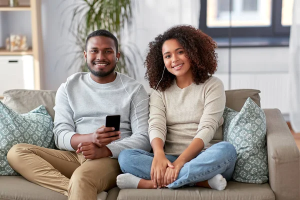 Casal feliz com smartphone e fones de ouvido em casa — Fotografia de Stock