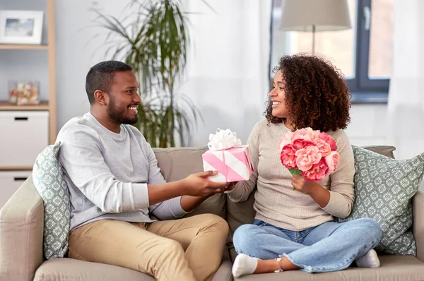 Feliz pareja con flores y regalo en casa — Foto de Stock