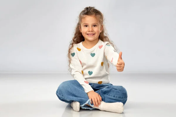 Little girl sitting on floor and showing thumbs up — Stock Photo, Image