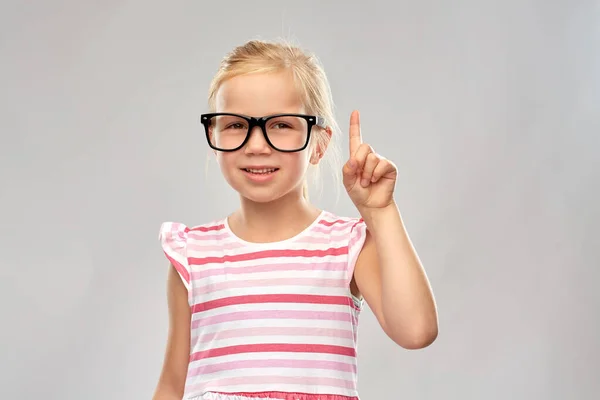 Niña sonriente en gafas apuntando con el dedo hacia arriba — Foto de Stock