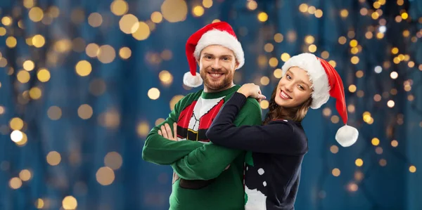 Happy couple in christmas sweaters and santa hats — Stock Photo, Image