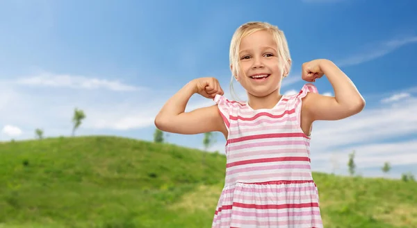 Glimlachend klein meisje tonen haar kracht in de zomer — Stockfoto