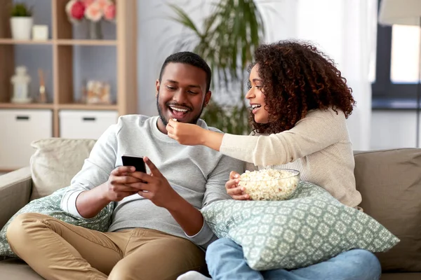 Pareja africana con palomitas de maíz y smartphone en casa — Foto de Stock