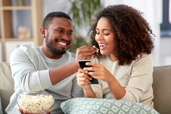 Afrikanskt par med popcorn och smartphone hemma — Stockfoto