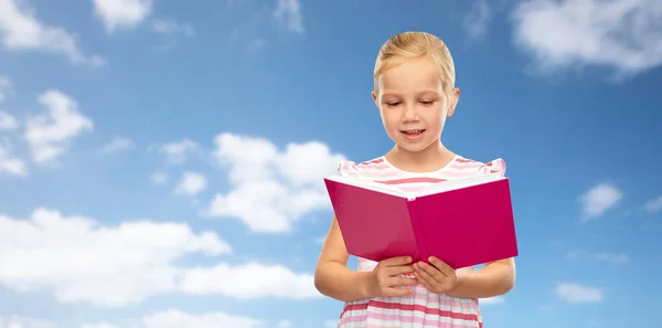 Kleines Mädchen liest Buch über Himmelshintergrund — Stockfoto