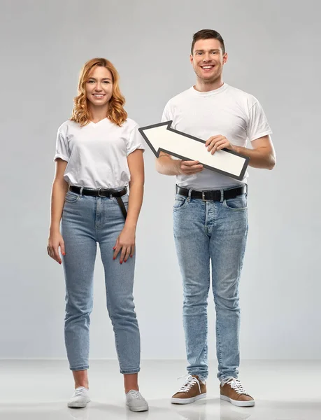 Happy couple in white t-shirts with arrow to left — Stock Photo, Image