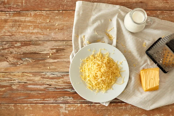 Close up of grated cheese and jug of milk on table — Stock Photo, Image