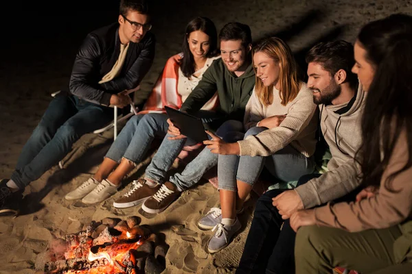 Amis avec tablette PC au feu sur la plage la nuit — Photo