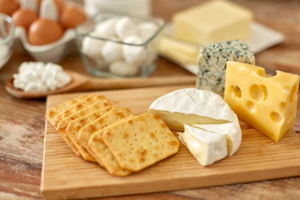 Crackers, cheese and other food on wooden board — ストック写真