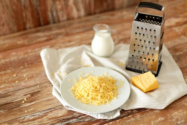 Primer plano de queso rallado y jarra de leche sobre la mesa — Foto de Stock