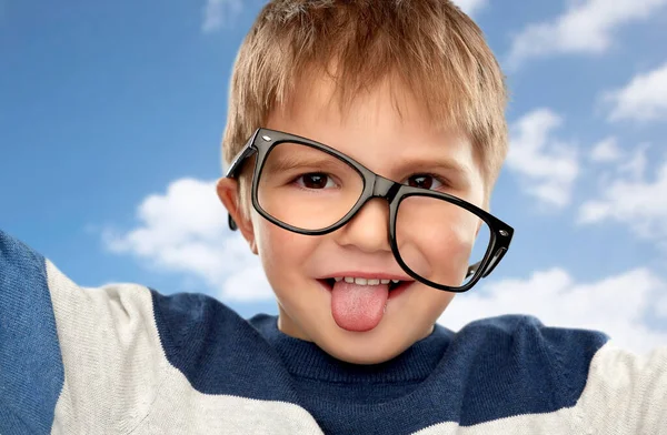 Портрет маленького мальчика в очках, показывающих язык — стоковое фото