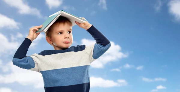 Маленький хлопчик з дахом книги на голові над небом — стокове фото