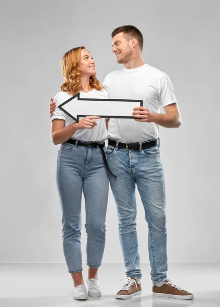 Feliz pareja en camisetas blancas con flecha a la izquierda — Foto de Stock