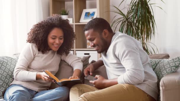 Glückliches Paar mit Smartphone und Buch zu Hause — Stockvideo