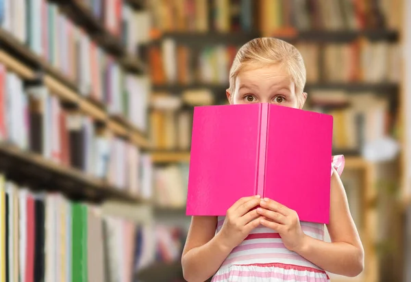 Menina se escondendo sobre livro na biblioteca — Fotografia de Stock