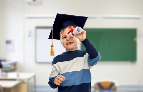 Niño pequeño en mortero mirando a través del diploma —  Fotos de Stock