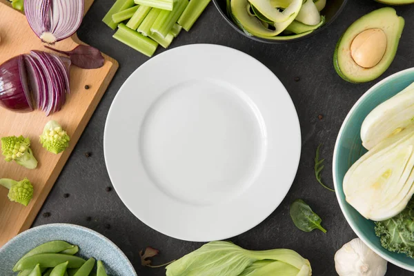 Different green vegetables and white empty plate — Stock Photo, Image