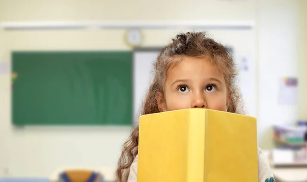 Menina se escondendo atrás do livro amarelo na escola — Fotografia de Stock