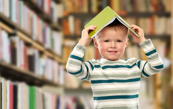 Lächelnder Junge mit Buch auf dem Kopf über Bibliothek — Stockfoto