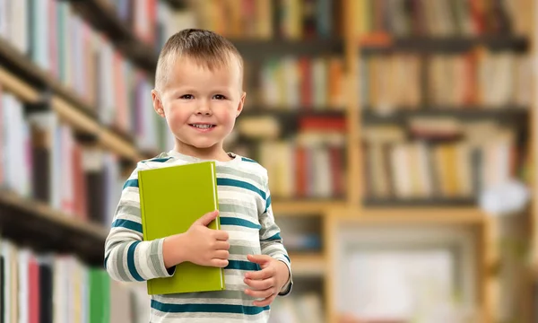 Πορτρέτο του χαμογελαστού αγοριού κρατώντας βιβλίο πάνω από τη βιβλιοθήκη — Φωτογραφία Αρχείου