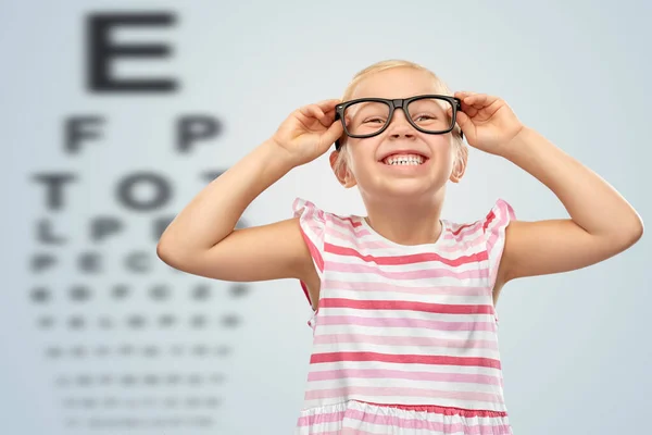 Mosolygós kislány szemüvegben a szemteszt diagram felett — Stock Fotó
