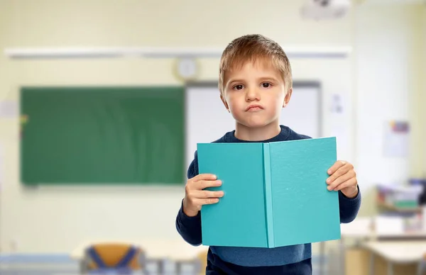 Missnöjd liten pojke med bok i skolan — Stockfoto