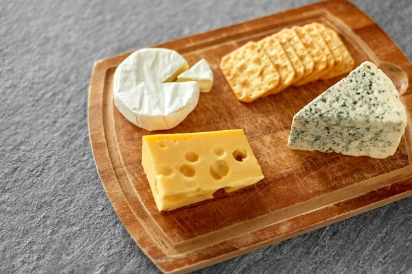 Diferentes queijos e biscoitos em tábua de madeira — Fotografia de Stock