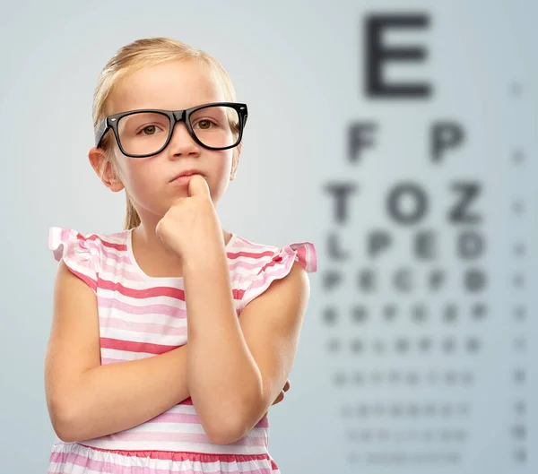 Liten flicka i glasögon över ögontest diagram — Stockfoto