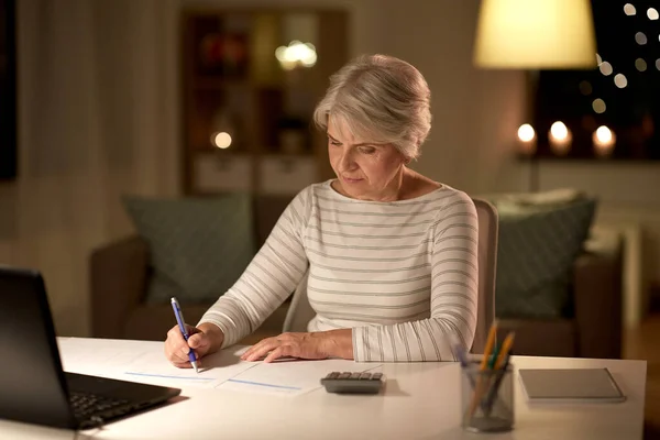 Femme âgée remplissant le formulaire d'impôt à la maison le soir — Photo