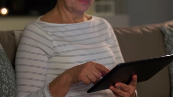 Счастливая пожилая женщина с планшетным компьютером дома по ночам — стоковое видео