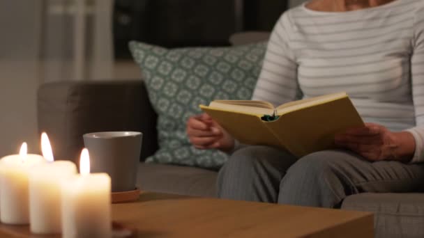 Старша жінка читає книгу і п'є чай вдома — стокове відео