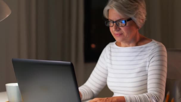 Akşam evde dizüstü bilgisayarı olan mutlu bir yaşlı kadın. — Stok video