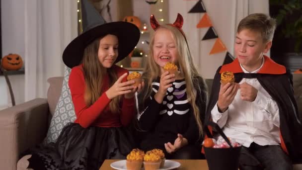 Děti v halloween kostýmy jíst cupcakes doma — Stock video