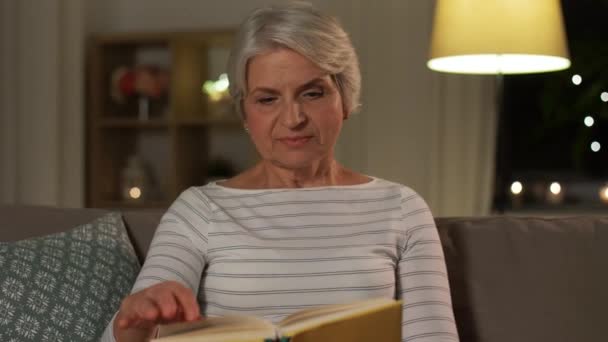 Wanita senior yang bahagia membaca buku di rumah di malam hari — Stok Video