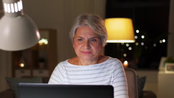 Счастливая пожилая женщина с ноутбуком дома вечером — стоковое видео