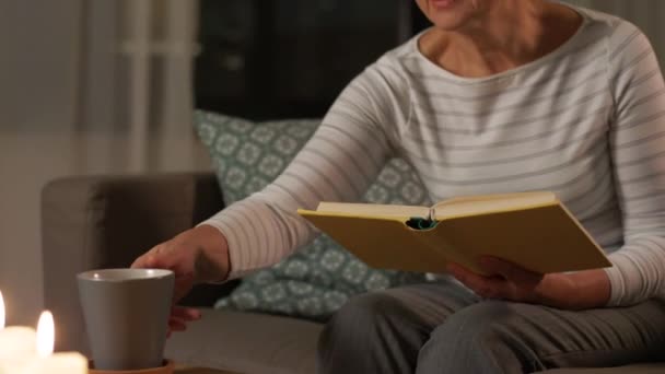 Старшая женщина читает книги и пьет чай дома — стоковое видео