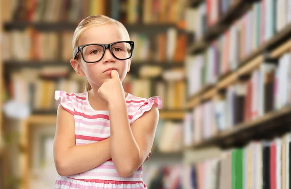 Liten flicka i svarta glasögon tänker på biblioteket — Stockfoto