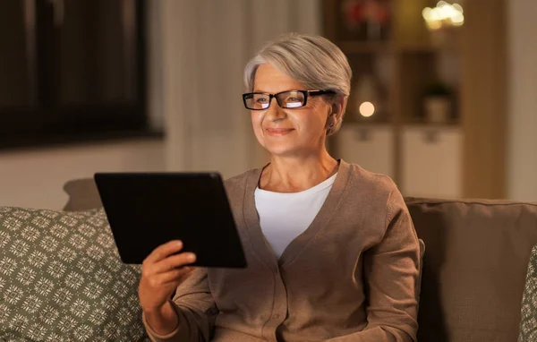 Heureuse femme âgée avec tablette pc à la maison la nuit — Photo