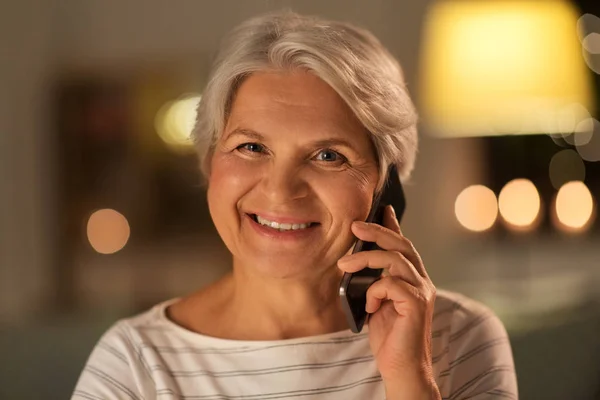 Пожилая женщина звонит на смартфон дома вечером — стоковое фото