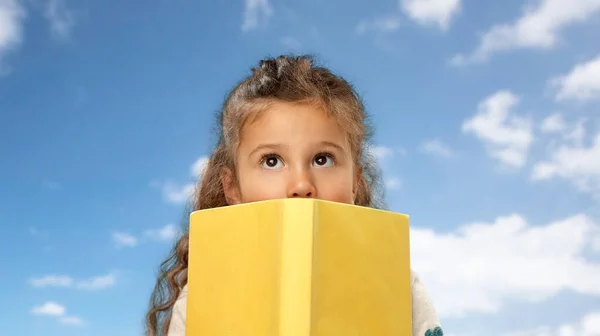 Petite fille cachée derrière livre jaune — Photo