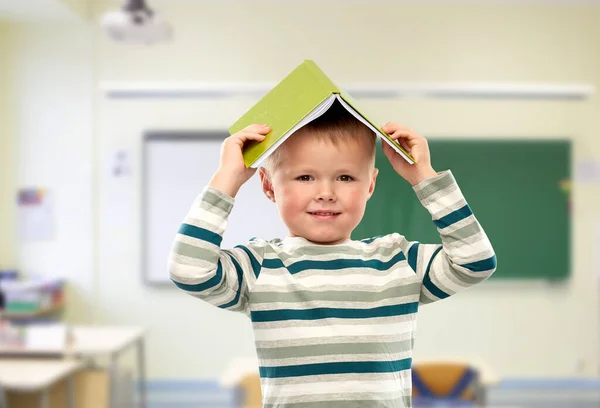 Leende pojke med bok om huvud i skolan — Stockfoto