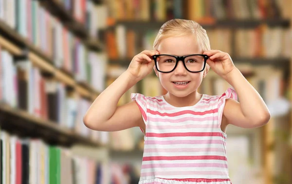Lächelndes kleines Mädchen mit schwarzer Brille in der Bibliothek — Stockfoto