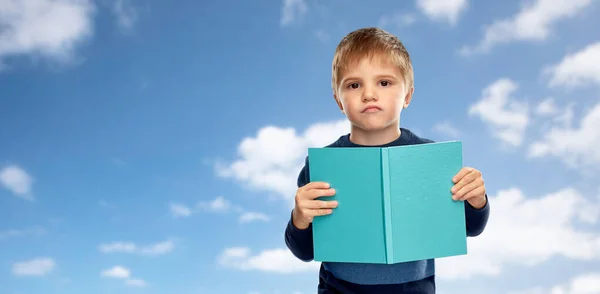 Незадоволений маленький хлопчик з книгою над блакитним небом — стокове фото
