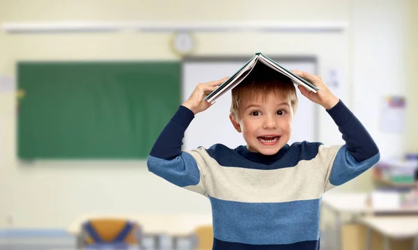 Petit garçon avec un livre sur la tête à l'école — Photo