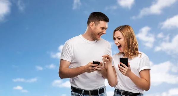 Feliz pareja en camisetas blancas con teléfonos inteligentes — Foto de Stock