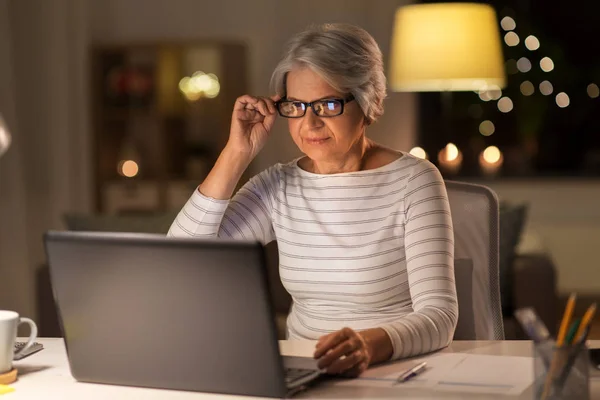 Старша жінка з ноутбуком працює вдома вночі — стокове фото