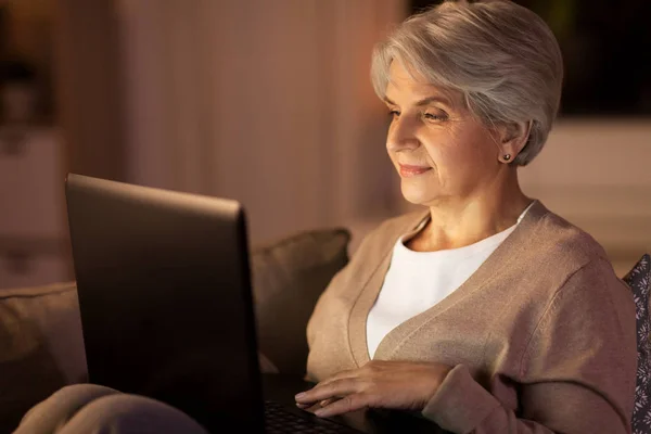 Счастливая пожилая женщина с ноутбуком дома по ночам — стоковое фото