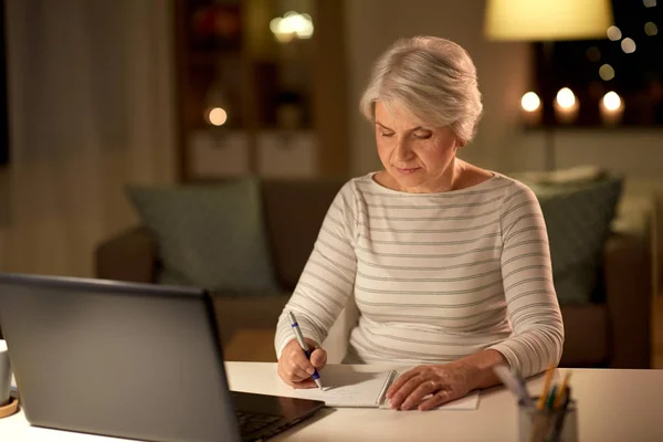 Seniorin schreibt nachts zu Hause an Notizbuch — Stockfoto